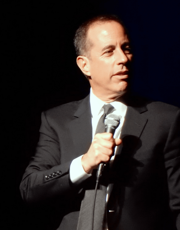Jerry Seinfeld holding a microphone while giving a speech