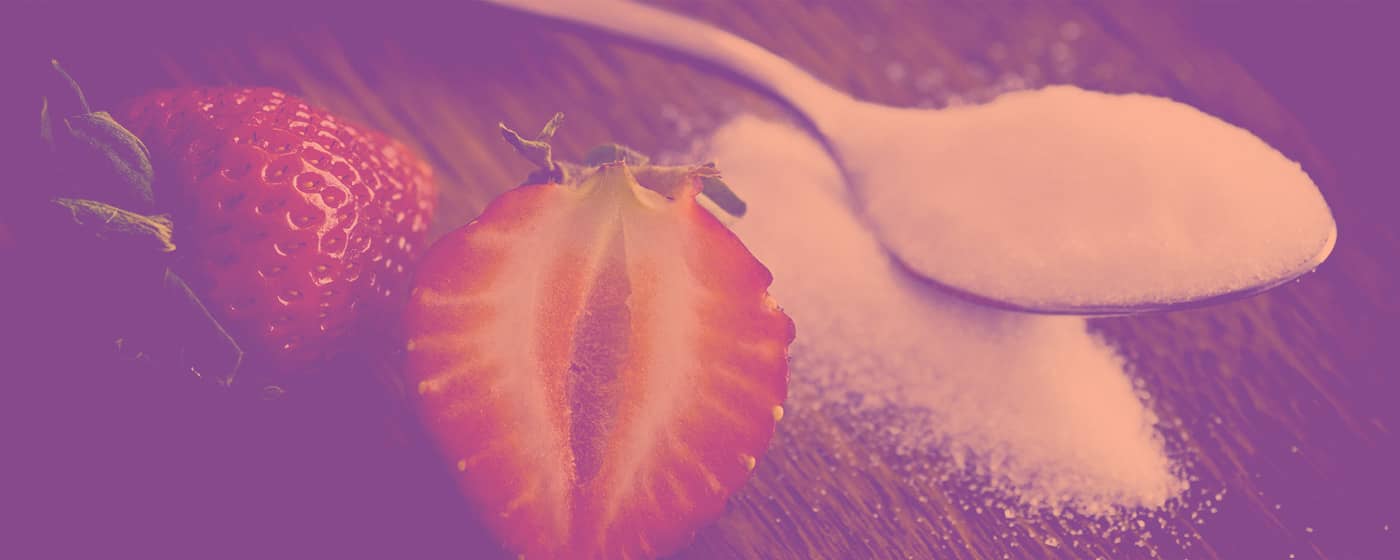 a sliced strawberry next to a spoonful of sugar
