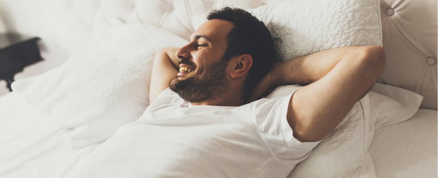 Man lying in bed with arms behind his head and smiling