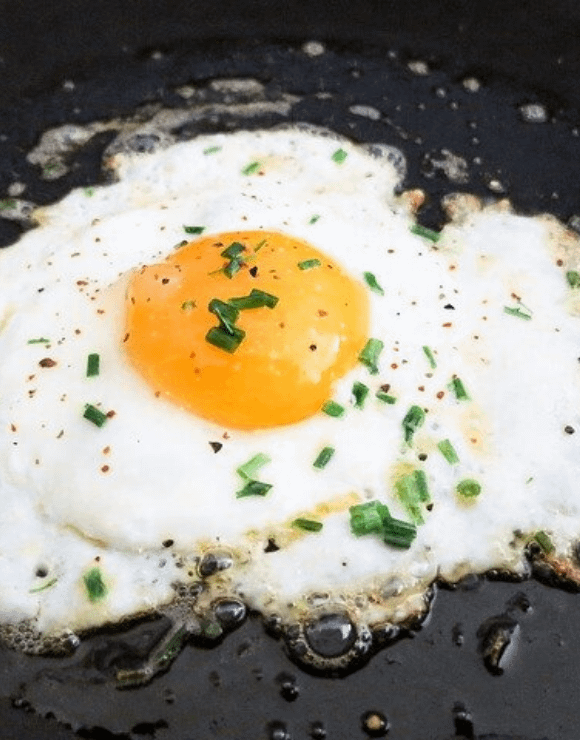A sizzling fried egg in a pan sprinkled with green onions