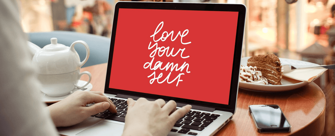 Woman typing on a laptop screen the words "Love Your Damn Self"