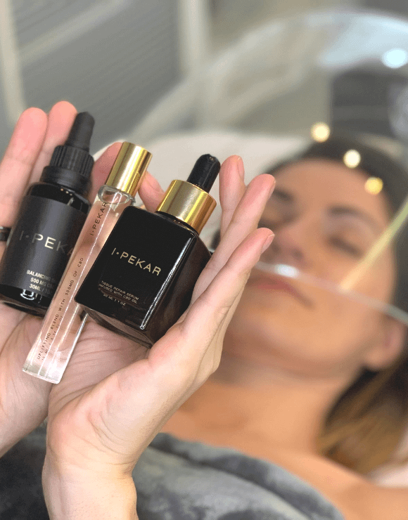 Woman receiving a cbd facial treatment while holding up cbd infused beauty products