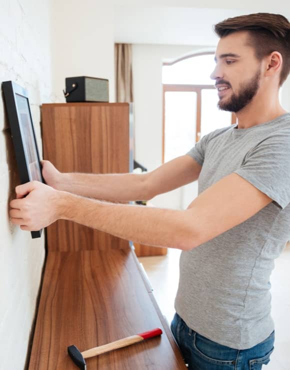 Man using life hack to hang picture from on brick wall