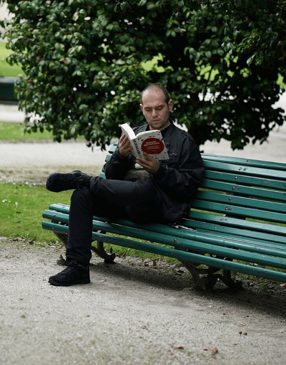 Man reads book on park bench about struggling with self-love